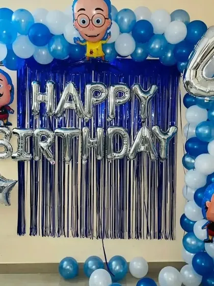 I can create decorations based on popular Indian cartoon characters as well. This setup for a 4th birthday includes a blue fringe backdrop, character foil balloons, and 'Happy Birthday' letter balloons.