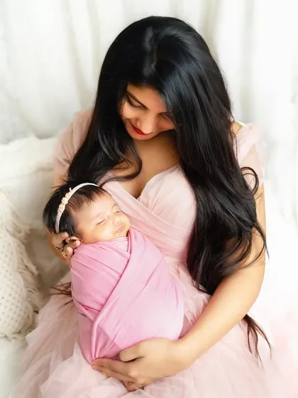 A mother's gentle smile as she holds her sleeping newborn. The soft pink tones of her dress and the baby's wrap create a warm and loving atmosphere.
