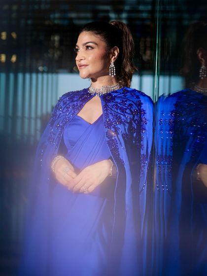 All eyes on this glamorous look. The client is wearing a stunning royal blue cape saree, and her makeup is equally dramatic, with bold eyes and a flawless base, perfect for a red-carpet-ready moment.