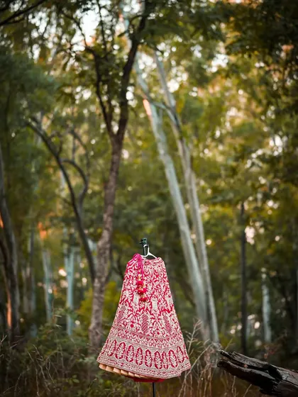 An artistic shot of the bridal lehenga displayed on a mannequin in a forest, contrasting the rich fabric with the natural environment.