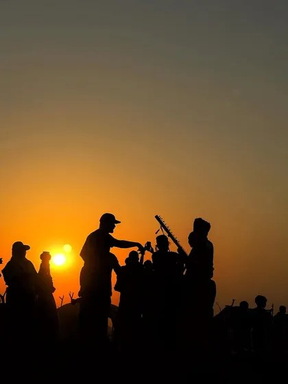A silhouette of musicians and onlookers at sunset. This captures the festive and communal atmosphere of the Pushkar Fair.