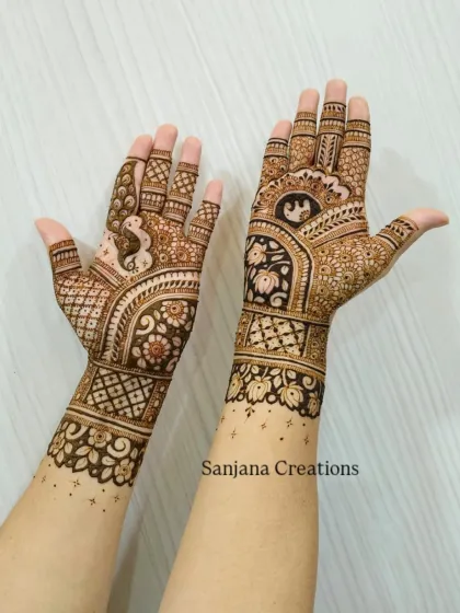 A unique take on bridal mehndi, with one arm showcasing a peacock and the other featuring an elephant, tied together with floral and geometric bands.