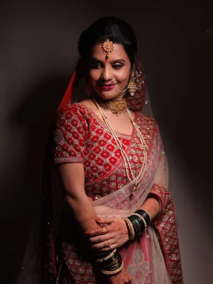 A portrait of our bride in a traditional red saree-style lehenga. The temple-style choker and jhumkas add a touch of South Indian grace to her look.
