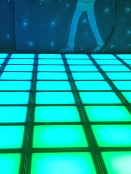The pixel dance floor glowing with a cool turquoise light, with silhouettes of dancers on the wall behind it.