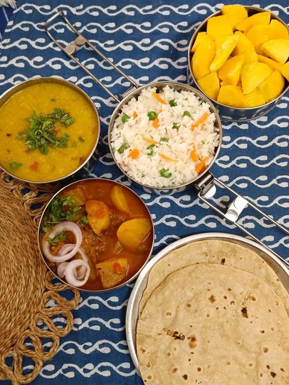 A complete meal featuring vegetable fried rice, aloo lauki ki sabzi, dal, and rotis, with a side of sweet ripe mango for a seasonal treat.