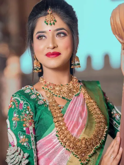 A bride wearing a pink and green saree, perfectly complemented by our antique finish temple jewellery set with green stone accents.