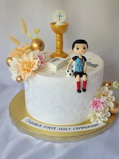 A First Holy Communion cake for Jason. The elegant white design is stenciled and decorated with a chalice, a Bible, and a figurine of the boy in his football jersey.