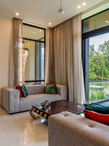 This view of the drawing lounge highlights the connection to the outdoors. The large glass windows frame the lush greenery, bringing the beauty of the farmhouse landscape right into the living space.