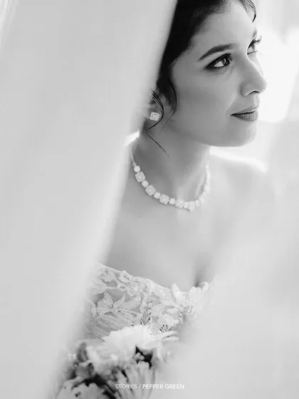 A soft-focus black and white portrait of the bride, framed by curtains, creating an artistic and pensive mood.