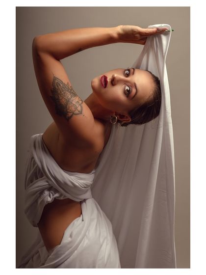 A fine art portrait with the model draped in white fabric. The pose is artistic and sculptural, creating a timeless and elegant image.