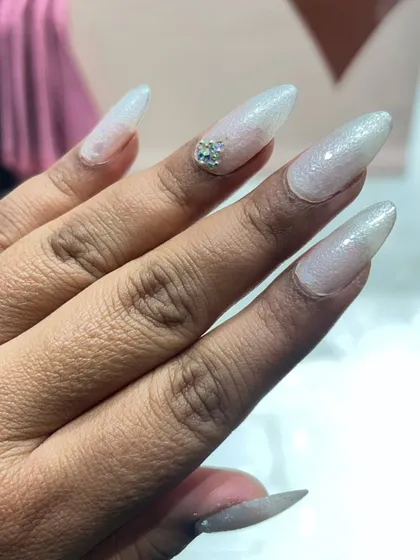 A close-up of our stiletto nail extensions with a shimmering iridescent finish. A small cluster of rhinestones at the base of the nail adds a perfect touch of glamour.