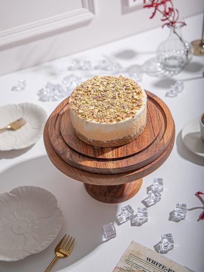 A pistachio-topped ice cream cake on a tiered wooden stand, surrounded by ice cubes to highlight its cool, refreshing nature.