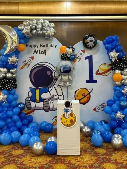 An outer space adventure theme for a first birthday, complete with an astronaut, moon and rocket ship balloons, and a planet-filled backdrop.