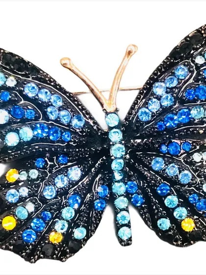 A stunning butterfly brooch featuring shades of blue and yellow stones on a black metal base. This accessory can add wings to your style, making a statement on any garment.