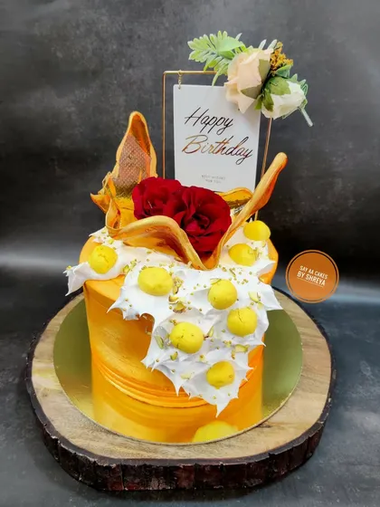 A celebration of nature's beauty, this cake features a warm yellow-orange buttercream base. It's decorated with a fresh red rose, meringue kisses, and artistic wafer paper sails.