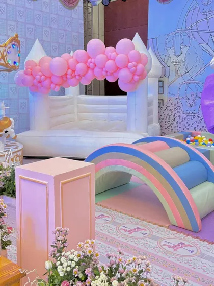 The dedicated soft play area, featuring a white bouncy castle, a pastel rainbow climber, and a ball pit, all thematically colored to blend seamlessly with the elegant party decor.