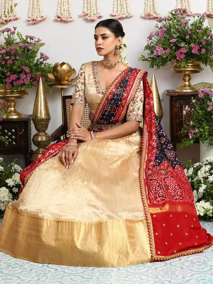 A seated view of the gold lehenga, showcasing the rich texture of the silk and the vibrant colors of the Bandhani dupatta.
