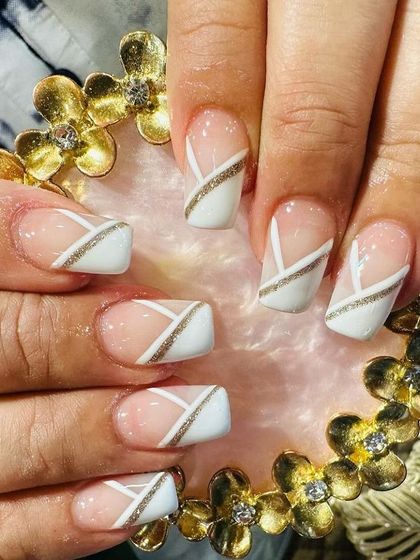 A geometric design using white blocks and gold glitter lines on square-shaped nails for a modern, architectural look.