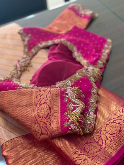 A pink blouse with peacock motifs and tassels on the sleeves.