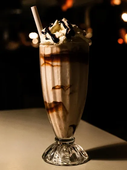 A classic diner-style milkshake. The dark, moody lighting with background bokeh makes it look like a scene from a movie.