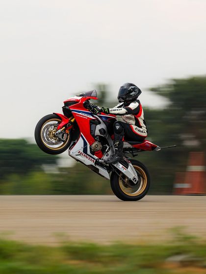 A rider on a red and white Honda CBR performs a graceful power wheelie. The smooth execution demonstrates a high level of skill.