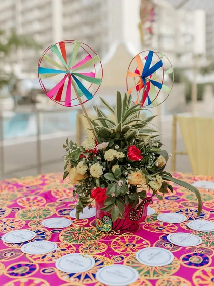 A whimsical centerpiece featuring fresh flowers and colorful pinwheels, adding a playful touch to the Haldi decor. The custom coasters add another layer of personalization.