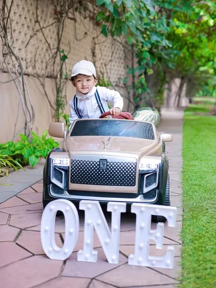 Cruising into year one. This outdoor shot combines a fun toy car prop with 'ONE' marquee letters for a stylish and modern first birthday portrait.