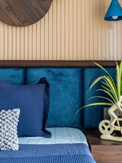 A close-up of the bedside in the blue-themed room, highlighting the playful bicycle-shaped planter and the texture of the headboard and wall paneling.