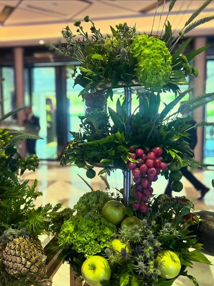 A detail shot showing how fruits like grapes and apples are incorporated directly into the tiered floral stands on the dessert table.