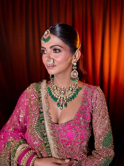 A raw, unedited shot of this royal bridal look. The focus is on the deep green and pink tones of the outfit, complemented by a classic smokey eye and flawless skin.