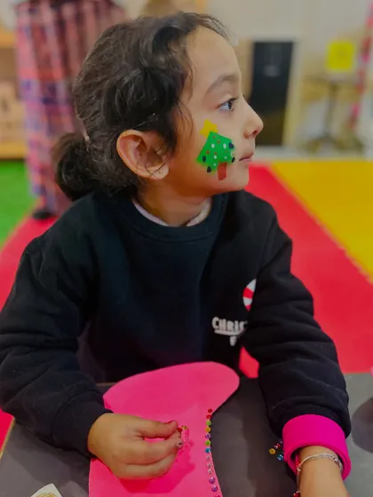 A student with a Christmas tree painted on her cheek is absorbed in her craft.