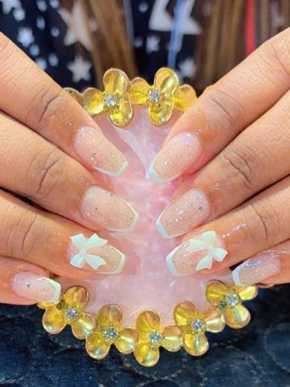 Coffin-shaped extensions with a modern French tip and delicate 3D white bows. The light glitter base adds a touch of sparkle to this clean design.