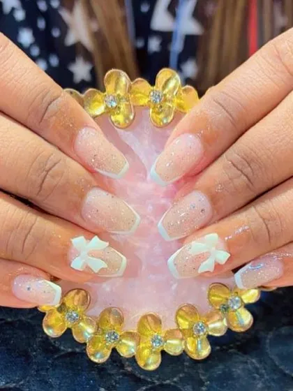 Coffin-shaped extensions with a modern French tip and delicate 3D white bows. The light glitter base adds a touch of sparkle to this clean design.