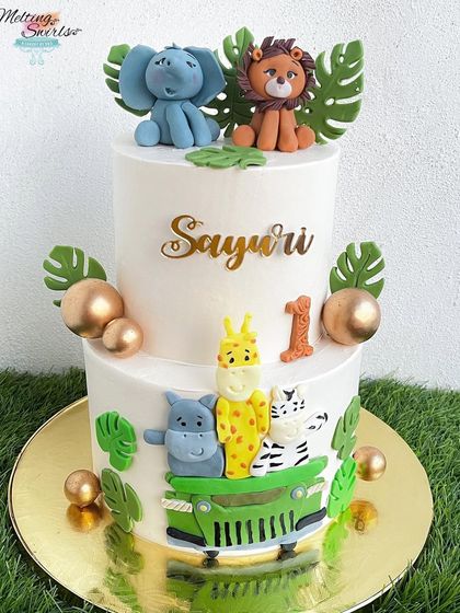 This two-tier jungle safari cake is perfect for a "Wild One" first birthday. It's decorated with a variety of handmade fondant animals, including a jeep full of critters, all on a clean, white whipped cream base.