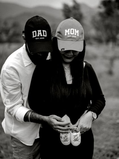 A tender black and white photo of the couple in their "Mom" and "Dad" caps, holding tiny baby shoes together over the bump.