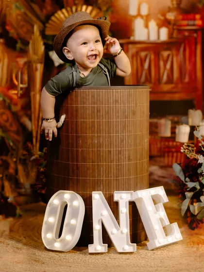 A joyful moment from a rustic-themed first birthday shoot, with the birthday boy smiling brightly from inside a prop barrel.