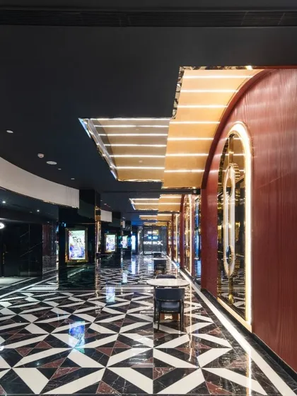 The main corridor at INOX Jalosa is a dynamic and glamorous passage. The design uses a bold, geometric floor pattern, reflective surfaces, and arched doorways with integrated lighting to guide patrons and build a sense of cinematic drama. The deep red leather-clad walls add a touch of classic theater opulence.