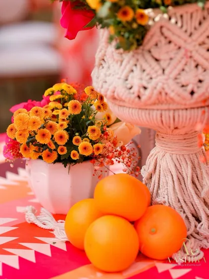 A close-up of the Haldi decor, featuring a vibrant mix of citrus oranges, macrame-wrapped vases, and colorful printed linens.