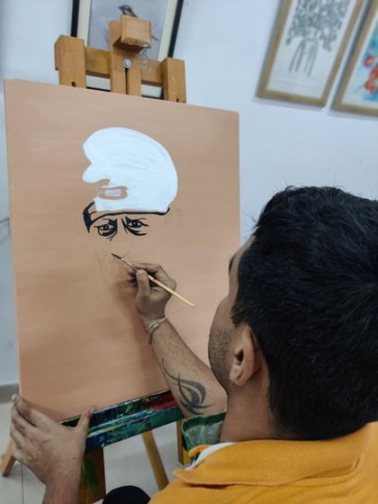 An adult student is captured through the process of painting a portrait of Sai Baba, showing concentration and devotion in his work.