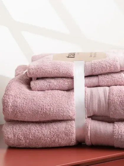 A set of pink towels, styled with a soap dispenser and diffuser. Adding other bathroom items creates a more complete and realistic lifestyle scene.