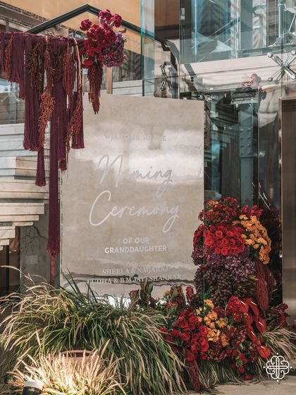 The welcome signage for the naming ceremony, framed by a dramatic and colorful floral installation.