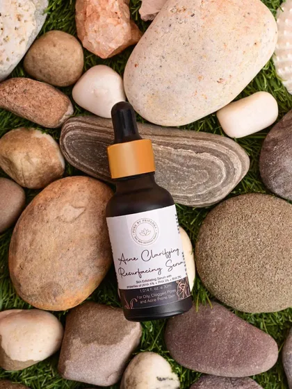 A flat lay of Pure by Priyanka's Acne Clarifying Serum on a bed of smooth river stones. This unique styling creates a feeling of natural purity and balance.