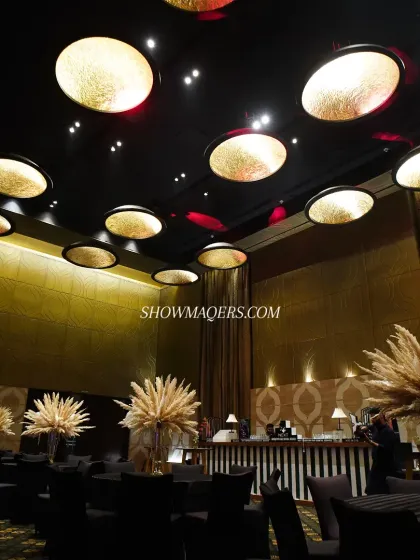 The ambiance of the masquerade-themed event, with dramatic ceiling lights, tall pampas grass centerpieces, and a black-and-white striped bar, all contributing to a cohesive and immersive theme.