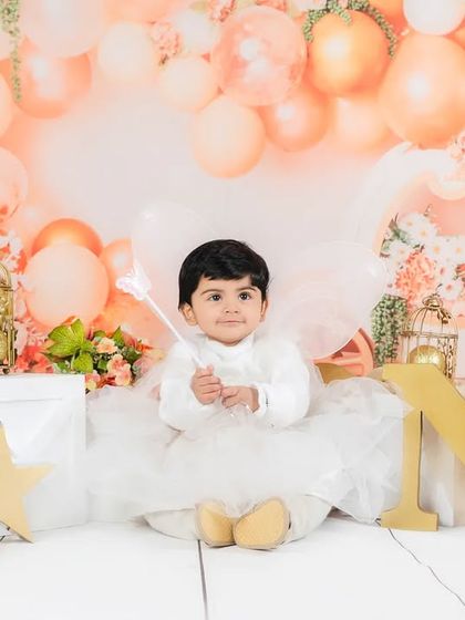 An angel-themed first birthday shoot, with the baby boy dressed in white with wings, sitting in front of "ONE" blocks.