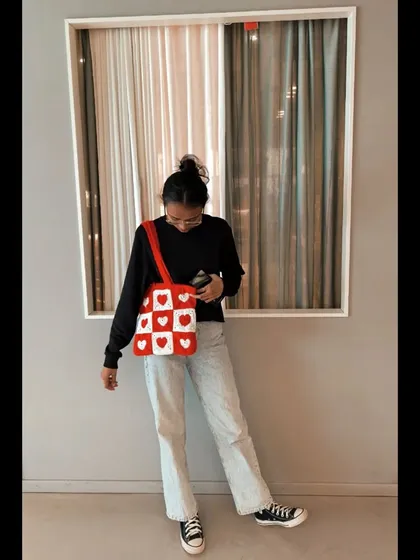 Rocking the crochet heart tote bag. It's a fun and playful accessory that adds a pop of color and personality to a simple jeans-and-sweatshirt outfit.
