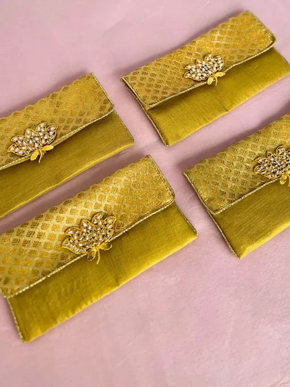 These elegant cash envelopes are made from a beautiful golden fabric and adorned with a kundan-style brooch. They are a luxurious way to present your shagun at a wedding.
