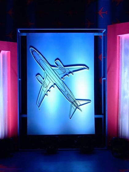 A travel-themed event backdrop featuring a large, backlit airplane silhouette.