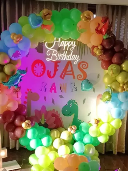 A "Roar-some" dinosaur-themed party for a 4th birthday. This setup includes a circular balloon arch in earthy tones, a custom backdrop with dinosaur graphics, and a light-up number '4'.