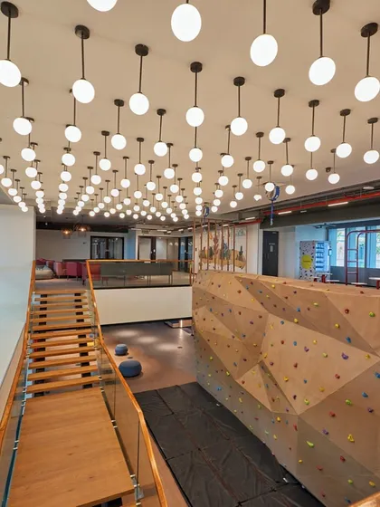 Work and play combined. We installed a rock-climbing wall as a central feature in this office, promoting an active and energetic company culture. The space is illuminated by a dramatic array of pendant lights.