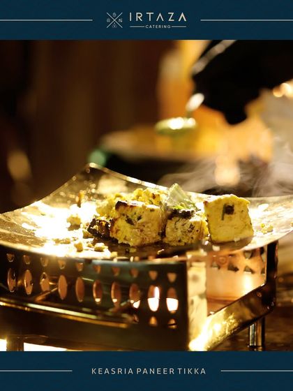 Sizzling Kesaria Paneer Tikka, infused with saffron and spices, served on a personal grill. The steam rising from the dish promises a hot and flavorful bite.